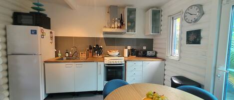 A compact kitchen with white cabinets, a stove, and a sink. There is a wooden table with a fruit bowl in the center.