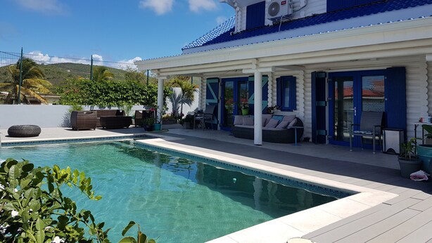 A poolside area with a clear pool, lounge chairs, and a covered seating area. - Stunning terraced Logcabin House with pool  (Saint Martin)