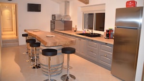 A modern kitchen with a wooden island, bar stools, stainless steel appliances, and a large refrigerator. - Large house 230m², 16 pers, private heated pool, 6000m² in the countryside (Nojals-et-Clotte)