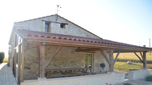 A stone building with a covered patio, a wooden bench, and a barbecue grill. - Large house 230m², 16 pers, private heated pool, 6000m² in the countryside (Nojals-et-Clotte)