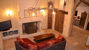 A living room with a fireplace, a sofa, a television, and a kitchen area visible through an open doorway. - Large house 230m², 16 pers, private heated pool, 6000m² in the countryside (Nojals-et-Clotte)
