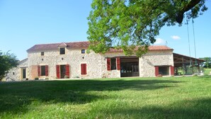 A stone building with a tiled roof, red shutters, and a covered porch. - Large house 230m², 16 pers, private heated pool, 6000m² in the countryside (Nojals-et-Clotte)
