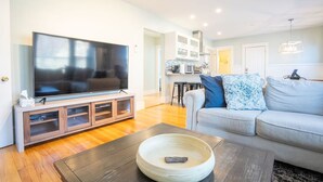 Ein Wohnzimmer mit Flachbildfernseher, einem Holztisch und einem hellen Sofa.