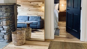 A modern living room with a large mirror, a stone fireplace, a blue sofa, and a wooden floor.