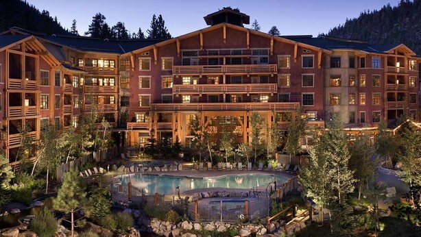 A large lodge with multiple balconies and a central pool surrounded by trees.