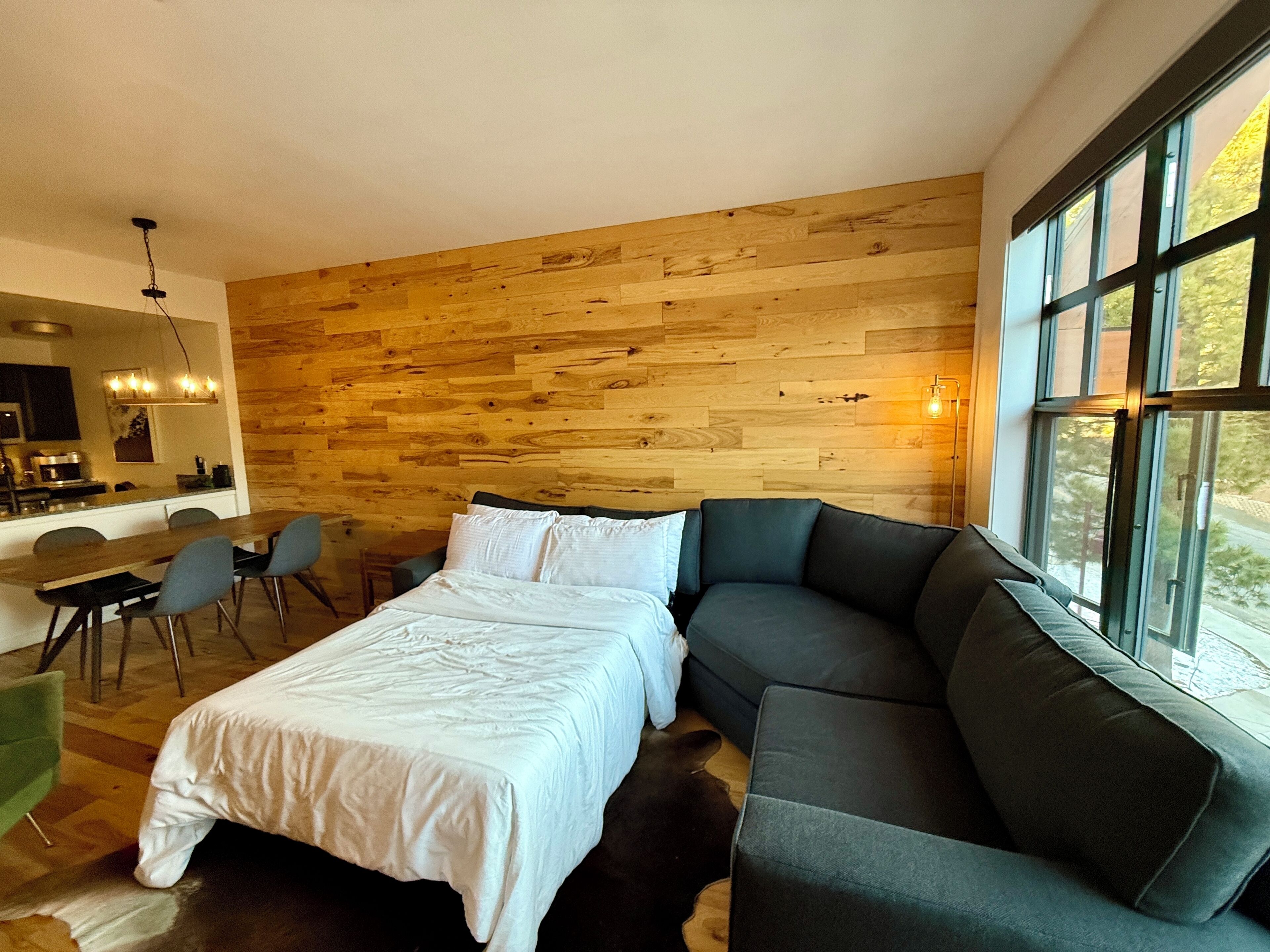 A modern room with a wooden wall, a bed, a sofa, a dining area, and a kitchen.