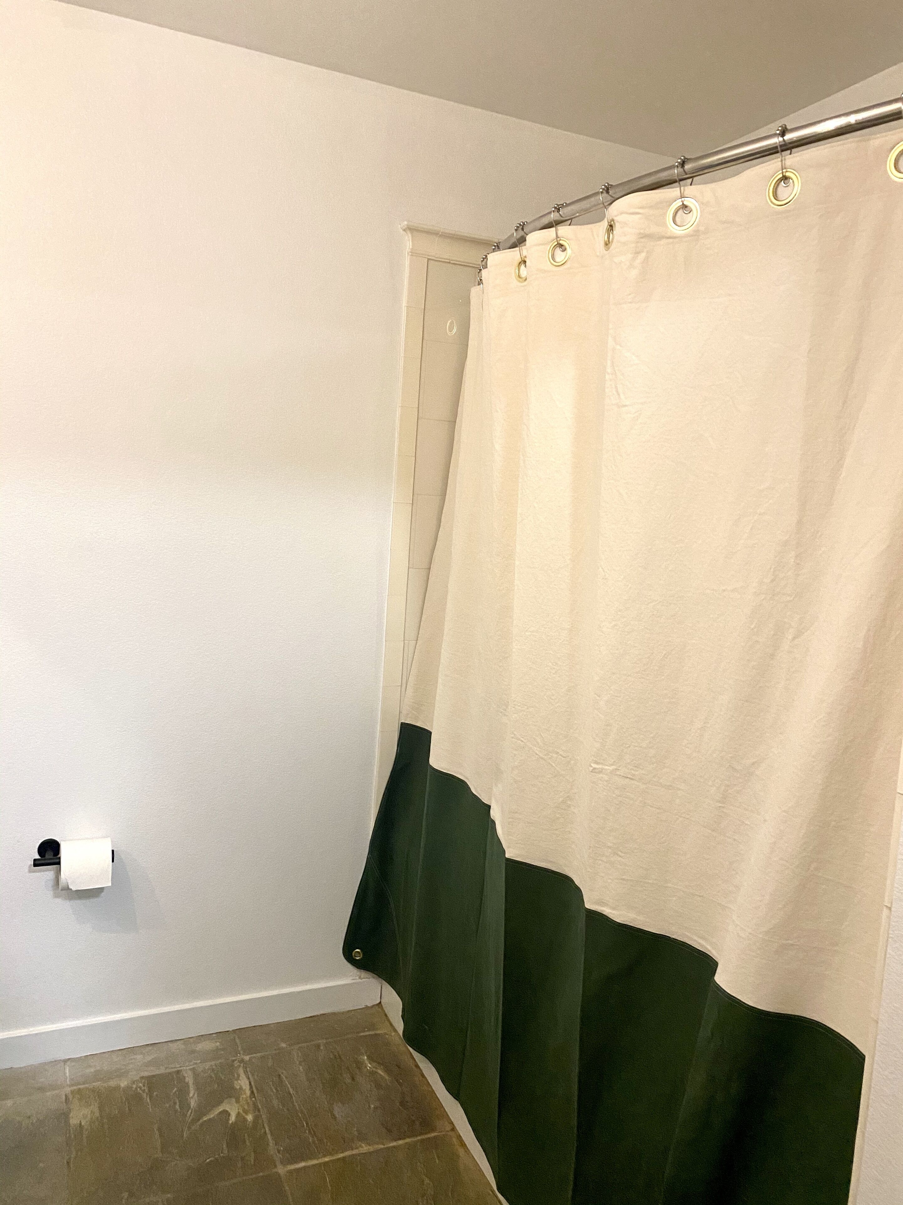 A bathroom with a shower curtain, a toilet paper holder, and a tiled floor.