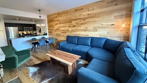 A modern living room with a sectional sofa, a dining area with a table and chairs, and a kitchen in the background.