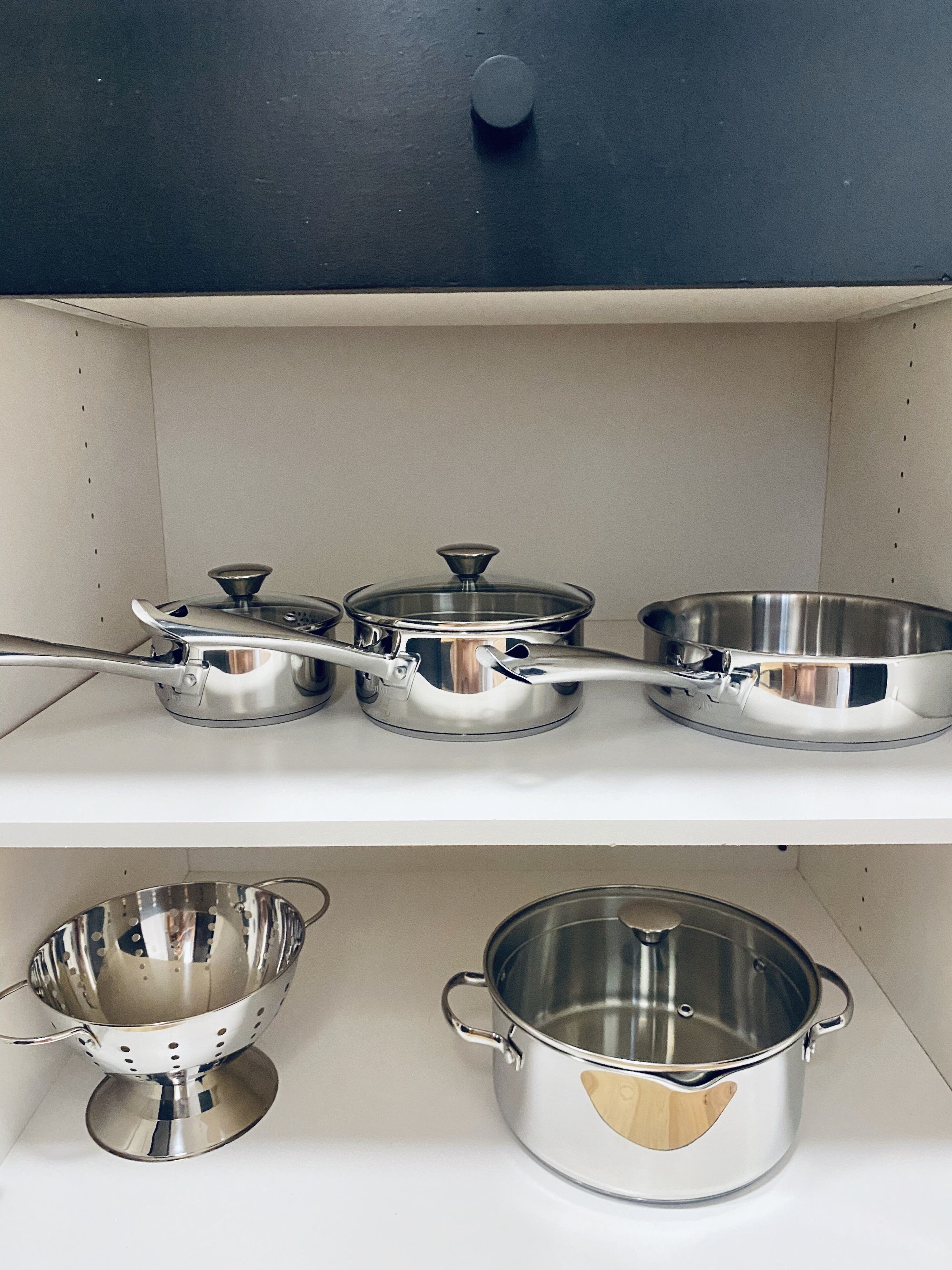 Una repisa de cocina con utensilios de acero inoxidable, incluyendo ollas, sartenes y un colador.
