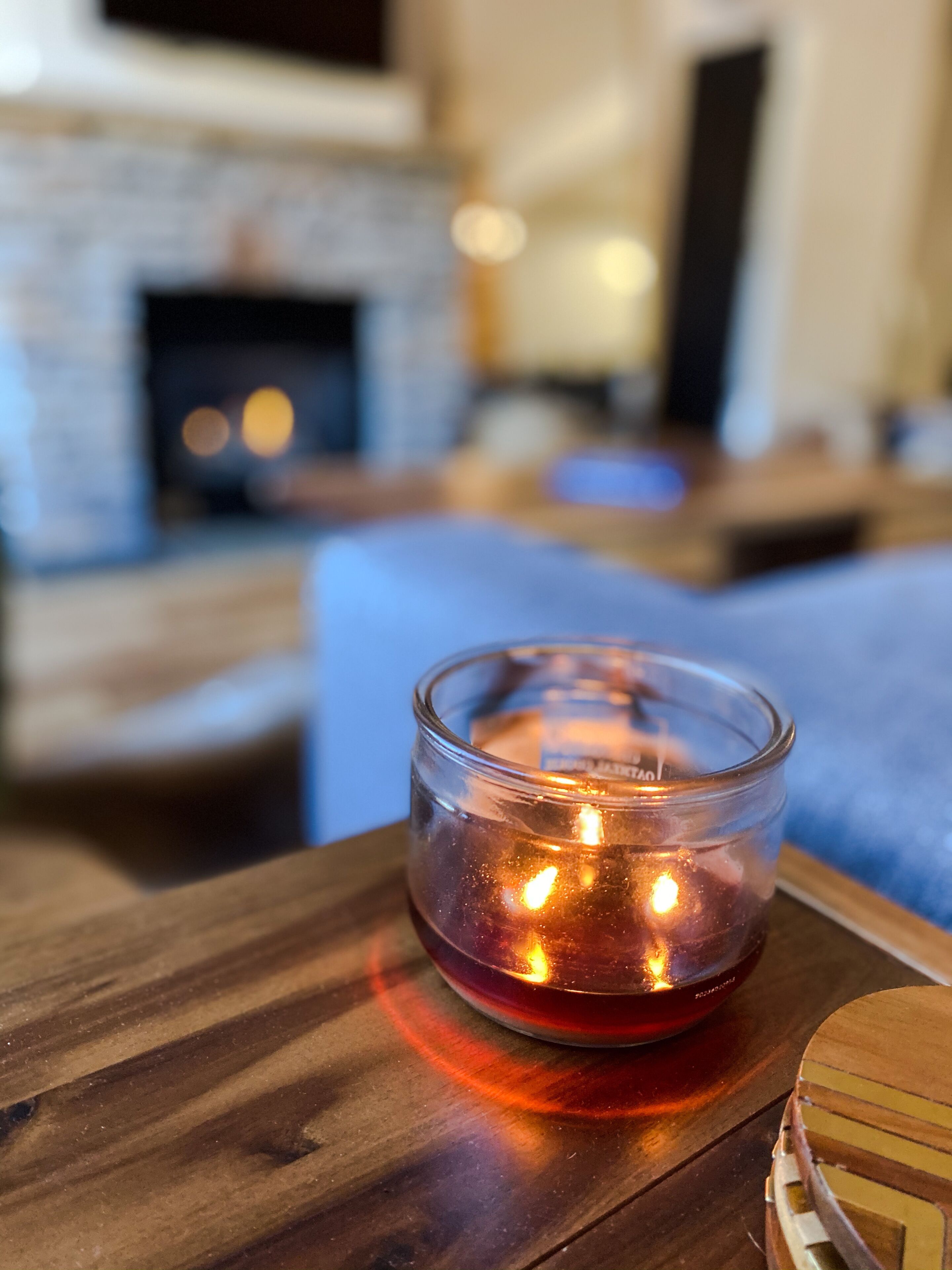 A glass candle holder with a lit candle on a wooden table in a living room.