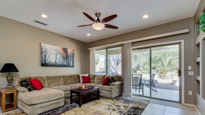 A living room with a sofa, armchairs, a coffee table, a floor lamp, a painting, and a view through a sliding glass door to an outdoor patio. - 3BR w walking trail, 45+ community, patio (Surprise)
