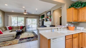 A spacious living area with a sofa, a coffee table, and a rug. There is a kitchen with wooden cabinets, a dishwasher, and a countertop with a sink. - 3BR w walking trail, 45+ community, patio (Surprise)