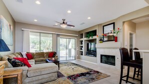 A spacious living room with a sofa, a coffee table, a fireplace, and a ceiling fan. - 3BR w walking trail, 45+ community, patio (Surprise)