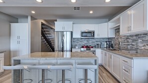 A modern kitchen with white cabinets, stainless steel appliances, a granite countertop, and a built-in island with bar stools. - Luxury Beachfront Six Palms Villas # 2 (puerto penasco)