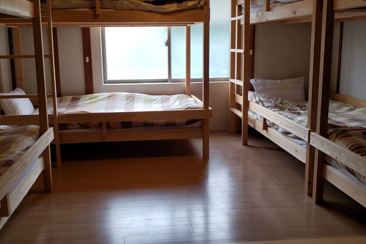 A dormitory room with bunk beds, a window, and wooden flooring.