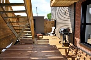A wooden deck with a staircase, a barbecue grill, and outdoor seating.