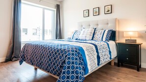 Ein Schlafzimmer mit einem großen Bett, einem Nachttisch, einem Fenster mit Vorhängen und drei gerahmten Bildern an der Wand.