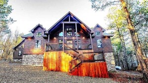 Una cabaña de troncos con base de piedra, una terraza de madera y una escalera que conduce a la entrada.