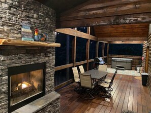 Un patio exterior acogedor con chimenea de piedra, terraza de madera y una mesa con sillas.