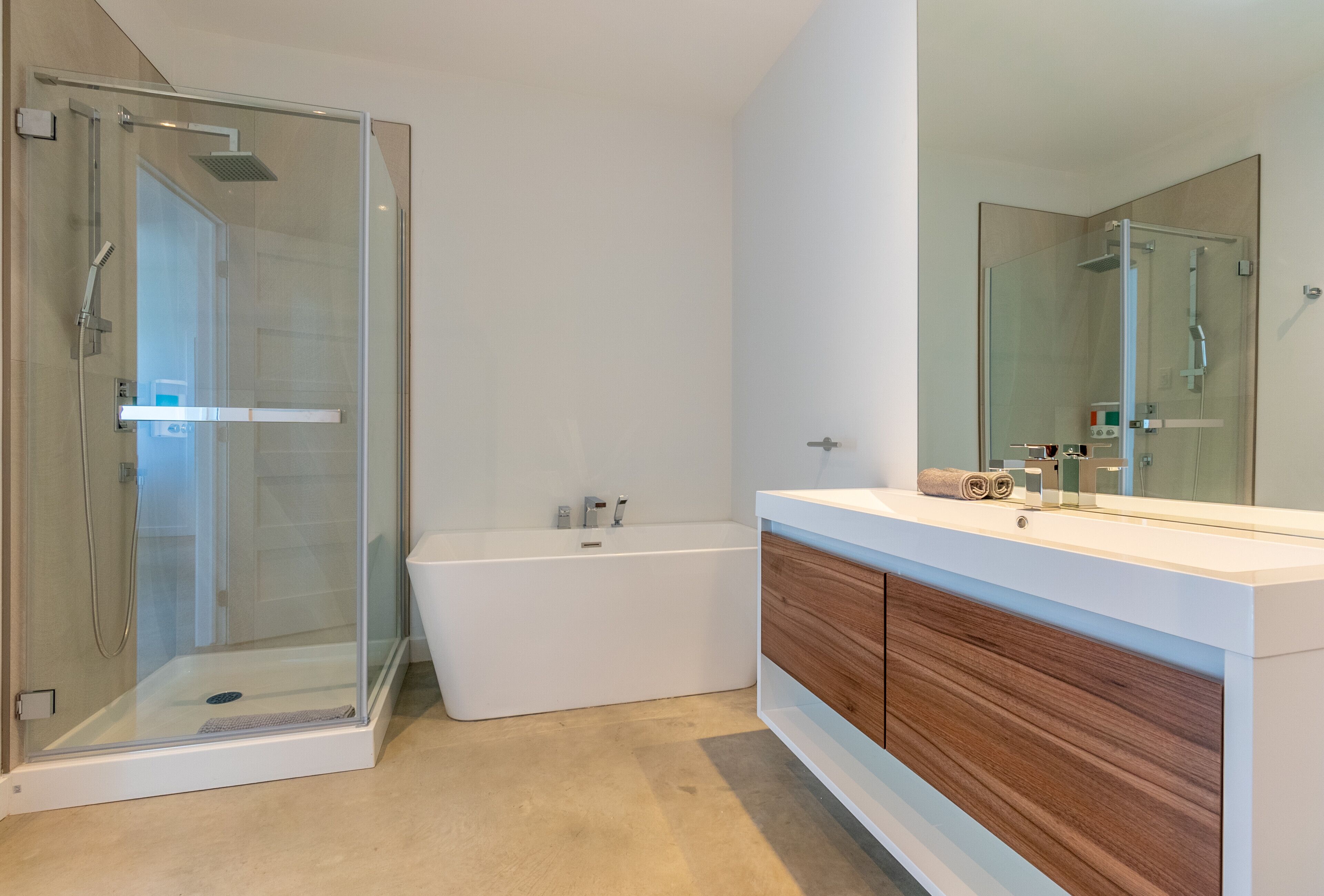 Un baño moderno con ducha envuelta en vidrio, una bañera independiente y un tocador con espejo.