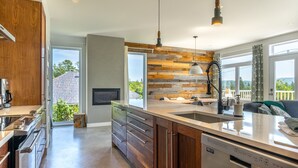 Une cuisine moderne avec des meubles en bois, un lave-vaisselle en acier inoxydable et une grande fenêtre donnant sur l’extérieur.