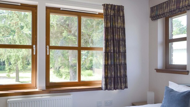 Quarto com cama, janela com cortinas e vista para árvores.