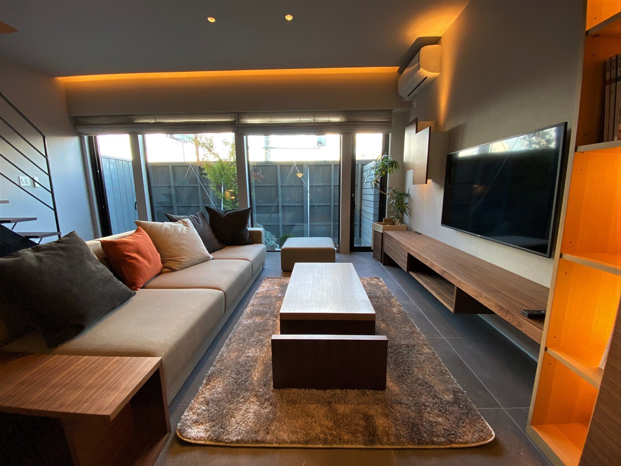 A modern living room with a sofa, coffee table, TV, and large windows.