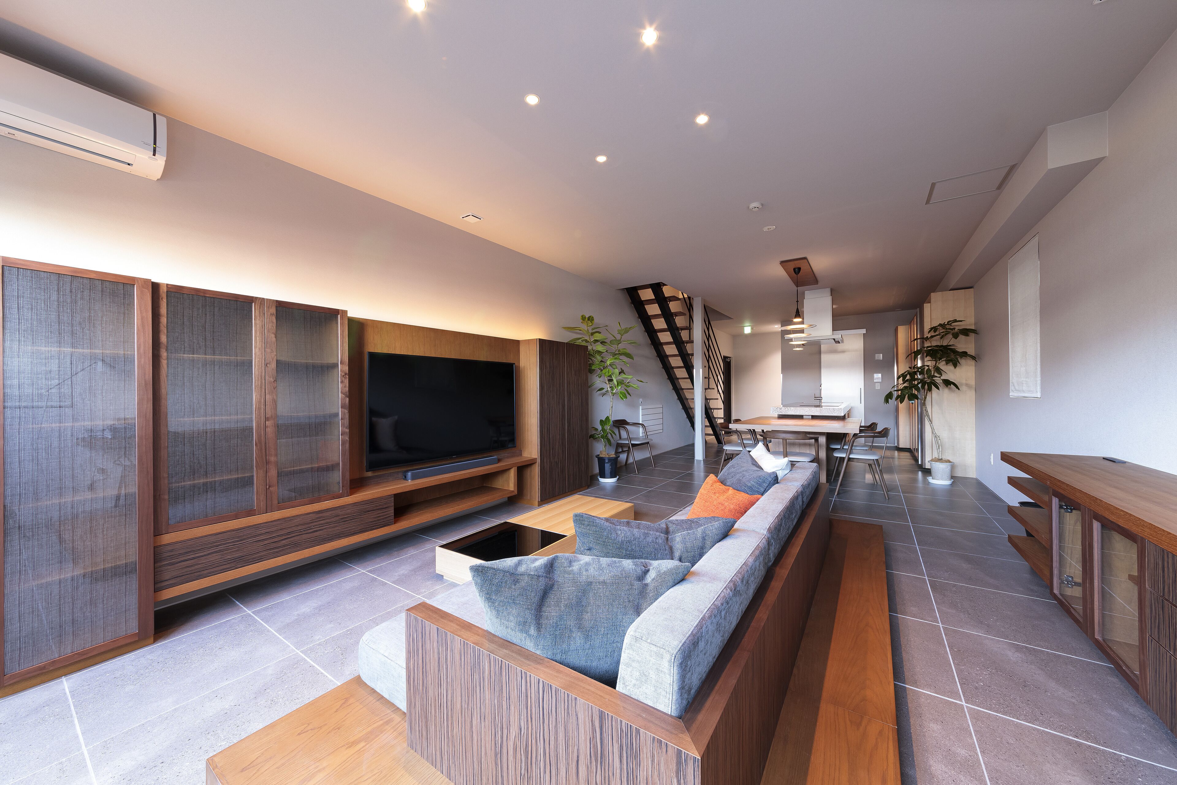Ein modernes Wohnzimmer mit einem großen Flachbildfernseher, einem Holztisch und einer eingebauten Couch mit Kissen.