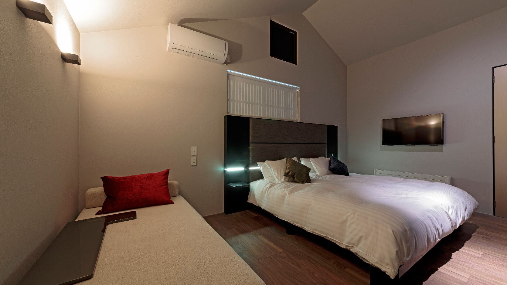 A modern bedroom with a bed, bedside tables, a TV, and an air conditioning unit.