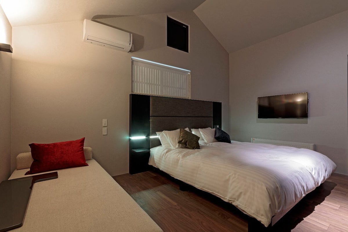 A modern bedroom with a bed, bedside tables, a TV, and an air conditioning unit.