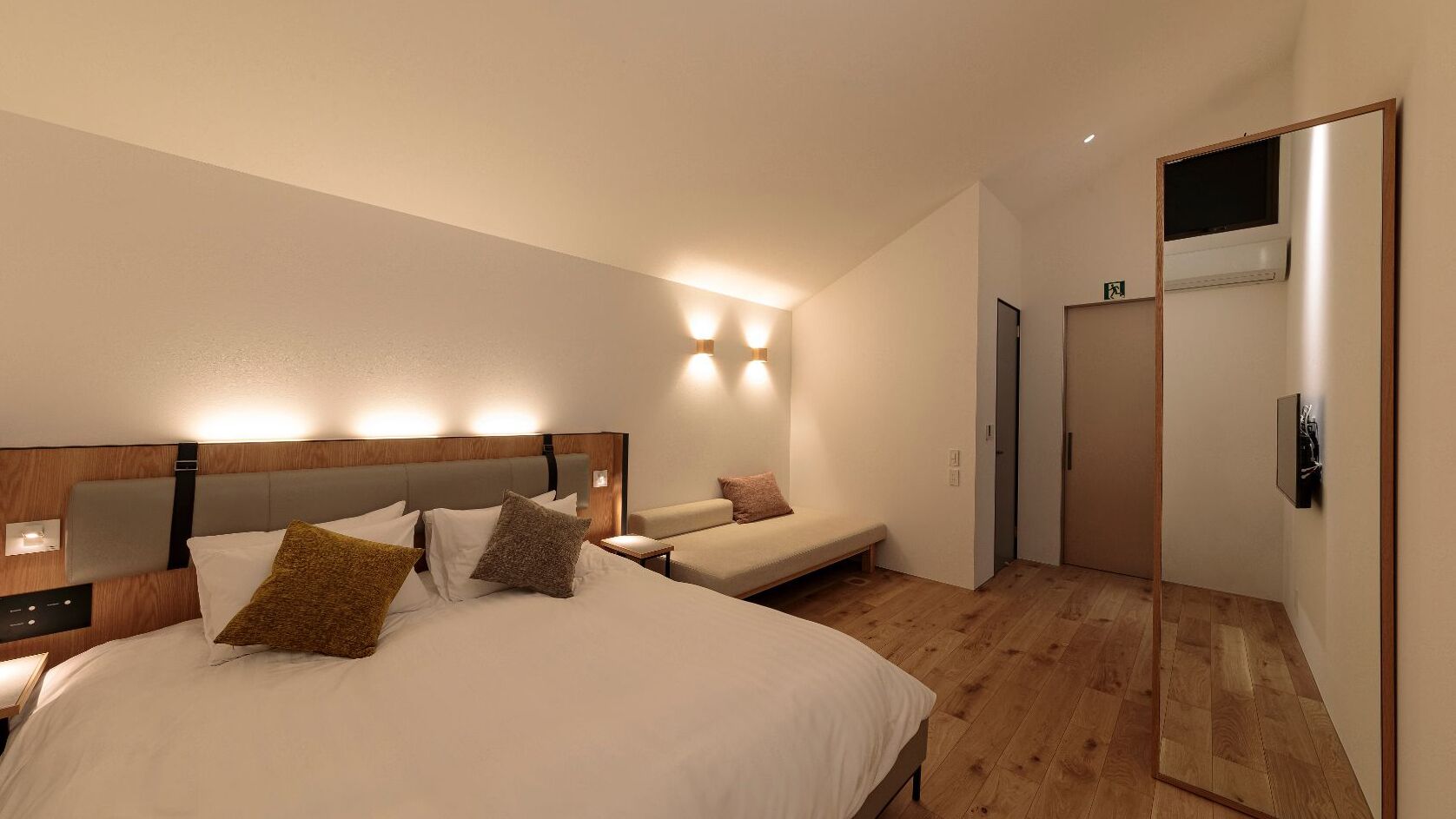 A hotel room with a large bed, a smaller bed, a bedside table, a mirror, and a door.