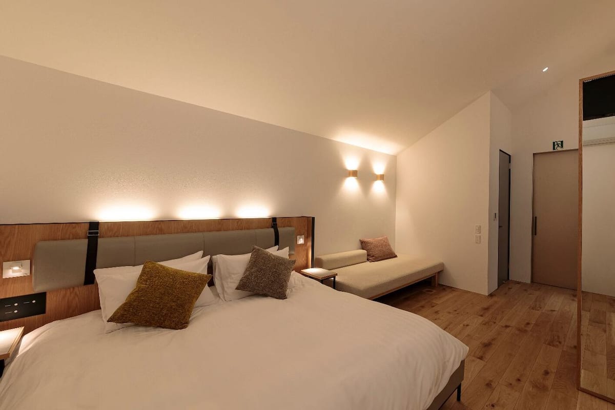 A hotel room with a large bed, a smaller bed, a bedside table, a mirror, and a door.