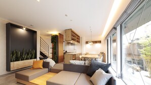 A modern living room with a sectional sofa, a kitchen area, and large windows. - Ishitei furano (Furano)