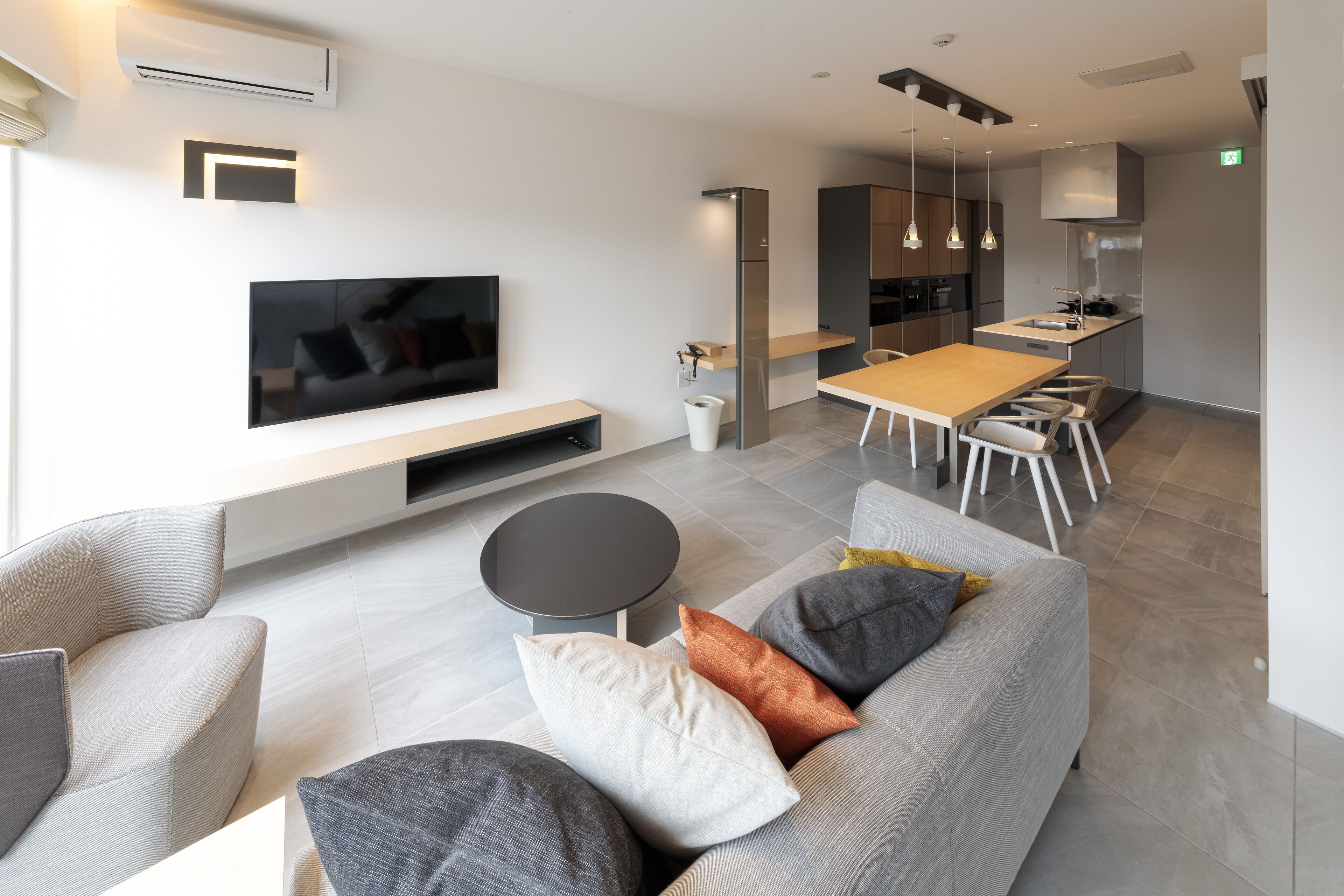 A modern living room with a flat-screen TV, grey sofa, and a dining area with a wooden table and chairs.
