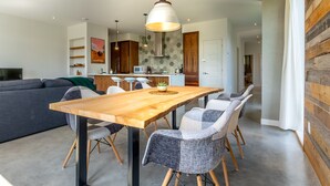 Ein moderner Essbereich mit Holztisch und -stühlen, einer hängenden Leuchte und einer Küche im Hintergrund.