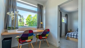 A bedroom with a bed, a desk with a chair, a window with curtains, and a potted plant.