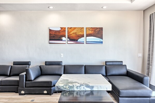 Un salon moderne avec un canapé d’angle, une table basse en marbre et deux tableaux accrochés au mur.