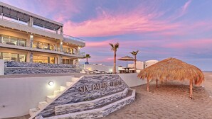 A hotel with a stone staircase leading to a pool area, a thatched umbrella, and a clear sky. - Luxury Beachfront Six Palms Villas # 4 (Puerto Penasco)