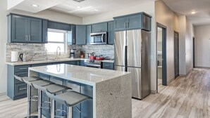A modern kitchen with dark blue cabinets, stainless steel appliances, and a granite island with bar stools. - Luxury Beachfront Six Palms Villas # 4 (Puerto Penasco)