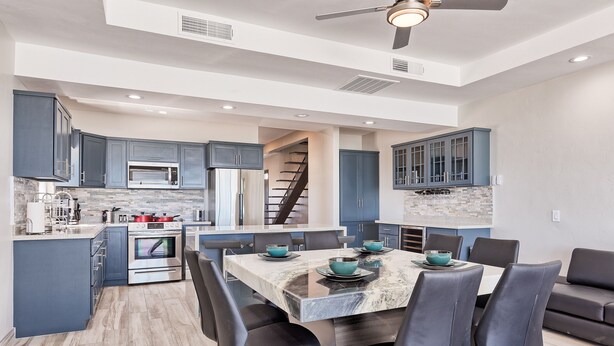 Una cocina moderna con armarios azul oscuro, una isla central con asientos, y una escalera que conduce a un nivel superior.