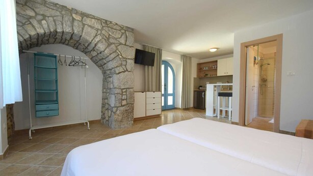 A bedroom with a stone archway, a bed, a wardrobe, a kitchenette, and a shower area. - Studio apartment Depope 1 (Skrbčići)