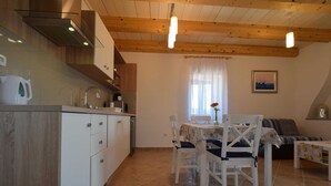 A kitchen with white cabinets, a wooden ceiling, and a dining area with a table and chairs. - Studio apartment Depope 2 (Skrbčići)