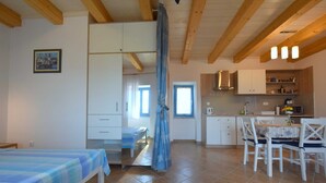 A room with a bed, a dining table with chairs, a kitchen area, and a bathroom with a shower curtain. - Studio apartment Depope 2 (Skrbčići)