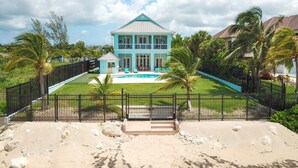 Un'ampia casa blu chiaro con piscina, circondata da un recinto nero e palme.