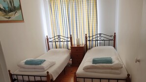 A room with two single beds, wooden floors, a painting on the wall, and a striped curtain.