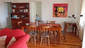 A cozy living room with a wooden dining table, chairs, a red sofa, a bookshelf, and a telescope on a tripod.