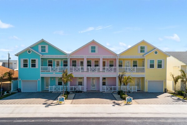 A three-story building with a central pink section and two side sections in blue and yellow. - Custom Coastal Retreat • Heated Pool & Hot Tub • 3 Min Walk to Beach (South Padre Island)