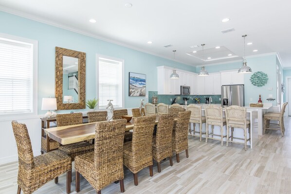 A spacious kitchen with white cabinets, a stainless steel refrigerator, and a dining area with wicker chairs and a wooden table. - Upscale Townhouse • Heated Pool & Hot Tub • Dog-Friendly (South Padre Island)