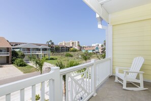 A balcony with a white chair, a view of a grassy area, and buildings in the background. - Upscale Townhouse • Heated Pool & Hot Tub • Dog-Friendly (South Padre Island)