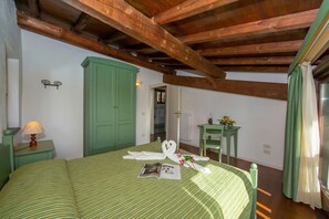 Una habitación con una cama, un armario verde, una mesita con una lámpara y una ventana con cortinas.